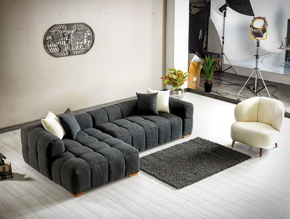 Ciemnoszara narożna sofa w nowoczesnym salonie z dużymi oknami.