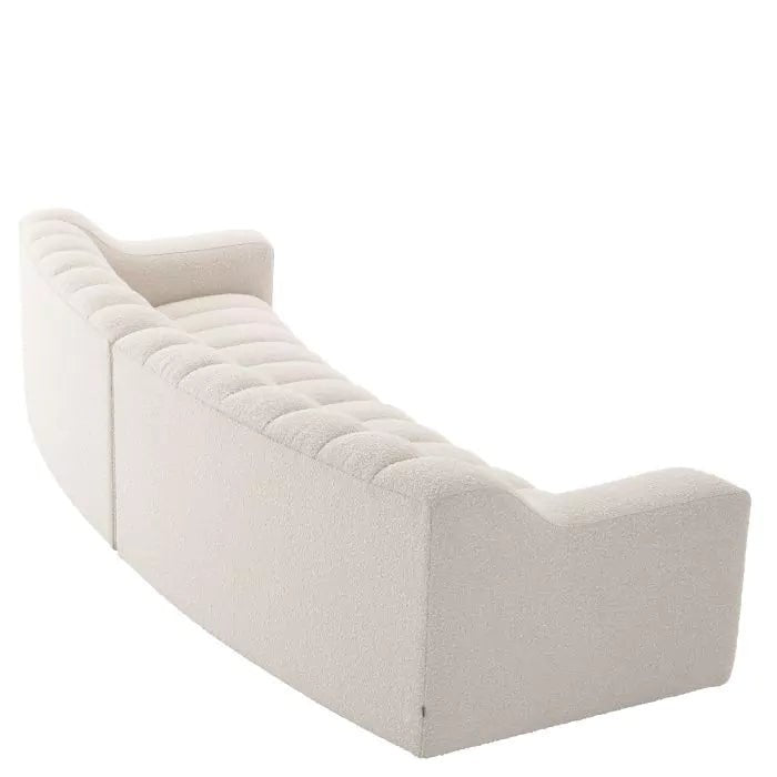 Beżowa, tapicerowana sofa o nowoczesnym, falistym kształcie z pionowymi przeszyciami.