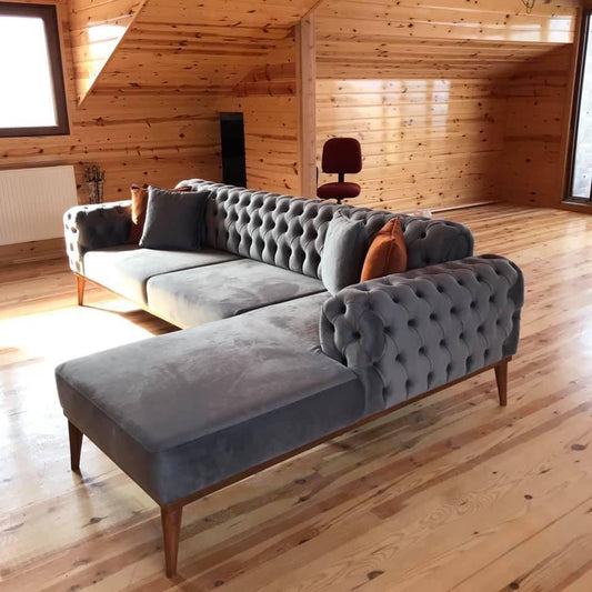 Szara sofa pikowana w rustykalnym salonie z drewnianą podłogą